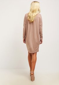 Langdrijke, knie-lange jurk van zachte, beige stof met een ontspannen pasvorm en een afgeronde zoom. Model draagt beige platformhakken.