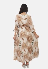 Maxi-jurk van doorschijnende stof met beige en bruine bloemenprint. Wijde mouwen en taille detail. De zoom reikt tot de enkel over doorzichtige blokhakken.