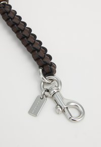 Brown and black braided leather strap with a silver metal clasp and a small rectangular tag engraved with "COACH."