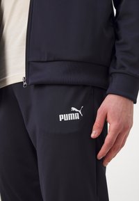 Jūras flotes sporta tērps, kurā ietilpst ar rāvējslēdzēju aizverama jaka un bikses. Audums ir gluds ar īsu spīdumu. Baltais Puma logo uz biksēm.