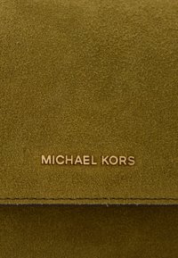 Zielono-oliwkowy zamsz o miękkiej teksturze. Posiada logo "MICHAEL KORS" w kolorze złotym. Czysty design z subtelnymi akcentami przeszycia.