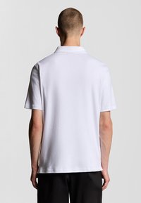 Weißes Poloshirt aus glattem Stoff, mit klassischem Kragen und kurzen Ärmeln, geradem Saum und minimalen Nähten.