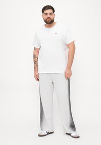 Hvit t-skjorte med korte ermer og rødt logo, kombinert med lysegrå joggebukser med svarte falmende detaljer og hvite treningssko.