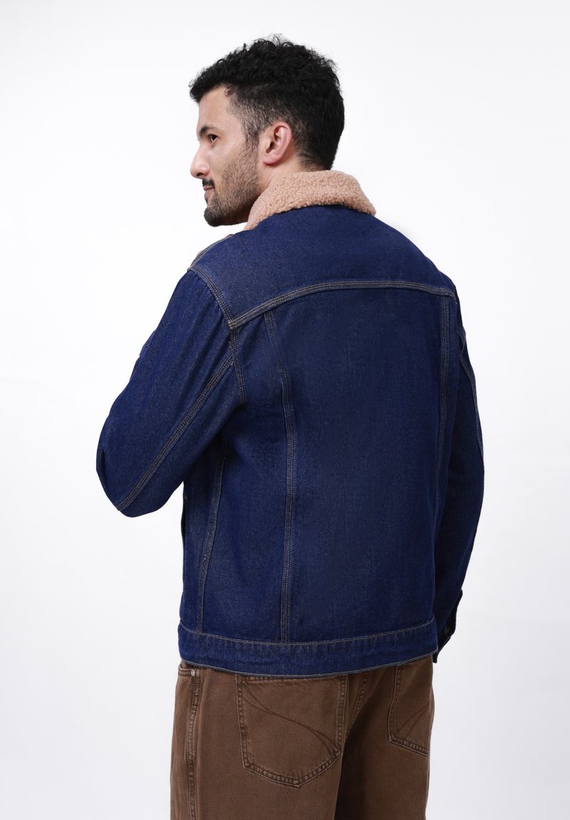 Veste en denim bleu foncé avec un col en fausse fourrure marron, présentant une coupe standard, des coutures visibles et des poignets boutonnés.