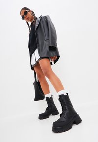 Botas de combate negras con plataforma y suela gruesa, diseño de cordones. La parte superior tiene una textura de cuero suave con detalle de cremallera lateral.