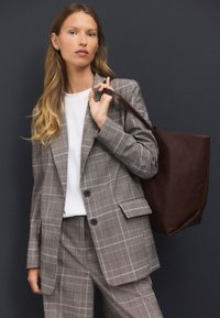 Gray plaid suit with a tailored blazer and matching trousers, paired with a white top and brown leather tote bag. Smooth texture, structured design.