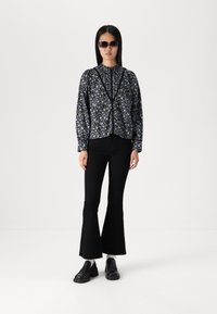 Blusa nera a maniche lunghe con motivo floreale, colletto tondo e chiusura con bottoni, abbinata a jeans neri svasati e scarpe nere chunky.