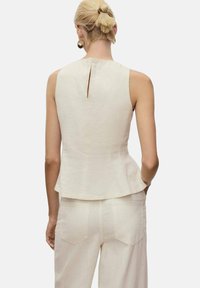 Helles beiges Peplum-Top aus Leinen, ausgestattet mit einem Schlüsselaugen-Ausschnitt im Rücken und nahtlosem Design. Kombiniert mit passenden Hosen.