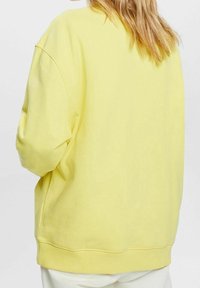 Žlutá mikina s volným střihem, spadlými rameny, žebrovanými manžetami a spodním lemem. Měkká textura s minimálním designem.