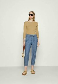 Camisola de manga longa bege, calças azuis às riscas com faixa elástica e cordão, sandálias bege e óculos de sol; design minimalista, aparência casual.