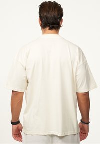 Hellbeige Baumwoll-T-Shirt mit kurzen Ärmeln, lockerer Passform und Rundhalsausschnitt, das minimalistische Nähte und keine sichtbaren Grafiken aufweist.