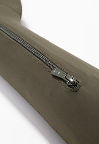 Manga de tela verde oliva con un prominente cierre metálico plateado en el lateral, con textura suave y detalles de costura reforzada.