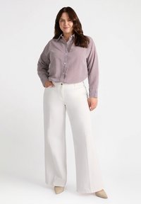 Camisa de botones a rayas en tonos rojos y blancos, combinada con pantalones anchos blancos. La camisa tiene un cuello con solapa y mangas largas.