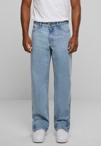 Jeans de mezclilla azul claro con un corte relajado, que cuentan con cinco bolsillos, presillas para el cinturón y una clásica cremallera de botón. Llevados con zapatillas blancas.