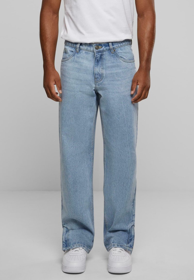 Jeans de mezclilla azul claro con un corte relajado, que cuentan con cinco bolsillos, presillas para el cinturón y una clásica cremallera de botón. Llevados con zapatillas blancas.