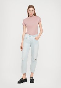 T-shirt aderente rosa chiaro con maniche corte, abbinato a jeans mom strappati blu chiaro. Mocassini neri completano l'outfit.