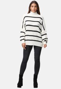 Kuscheliger Strickpullover in Weiß mit schwarzen horizontalen Streifen, hohem Kragen und übergroßer Passform, kombiniert mit schwarzen Skinny Jeans und Ankle Boots.