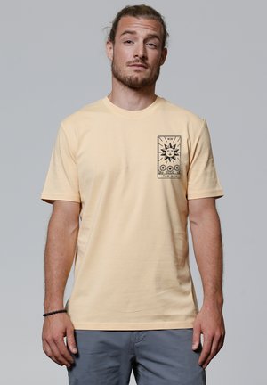 Geel katoenen t-shirt met korte mouwen, ronde hals en een zwarte grafische print met een zon en bloemen op de linkerkant van de borst.