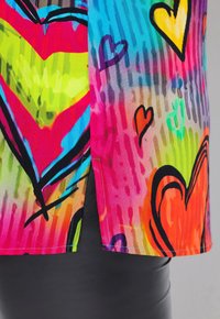 Tessuto colorato e multicolore con forme cuori di varie dimensioni. Include una fessura laterale e un design astratto audace con tonalità vivaci.