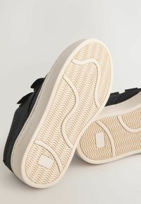 Schwarze Sneakers mit einem strukturierten Stoff-Obermaterial, einer gummierten Laufsohle mit einem gewellten Muster und flachem Absatz, die für Komfort und Grip ausgelegt sind.