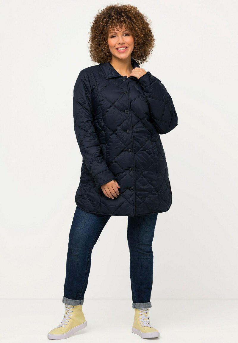 Navy prošívaný kabát s knoflíkovým zapínáním, klopovým límcem a dlouhými rukávy, spárovaný s džíny a světlezelenými vysokými teniskami.