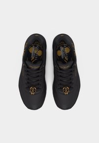 Μαύρα αθλητικά παπούτσια Skechers με χρυσά κορδόνια σε σχήμα κρανίου και χρυσή διακόσμηση, που διαθέτουν ενδιάμεσα πέλματα από αφρό μνήμης με σχέδιο σκελετού ποδιού.