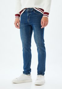 Niebieskie dżinsy z dopasowanym krojem, z klasycznym pięciokieszeniowym designem, przeszyciami oraz lekko wypłowiałym wykończeniem, połączone z białymi trampkami.