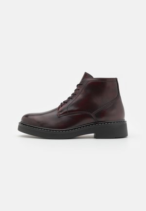 Bottine en cuir bordeaux avec une finition lisse, au design à lacets, à bout rond et semelle en caoutchouc noir avec des détails de couture.