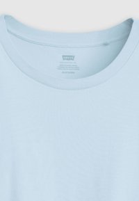 T-shirt en coton bleu clair avec un col rond et un col côtelé, présentant une étiquette avec les informations de la marque et d'entretien à l'intérieur du col.
