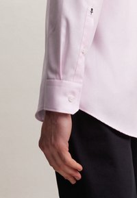 Camicia rosa chiaro con finitura testurizzata, caratterizzata da un polsino con bottone e un piccolo dettaglio ricamato in nero sulla manica. Vestibilità slim.