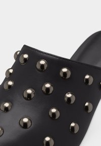 Chaussure noire en cuir sans lacets avec des clous métalliques ronds couvrant uniformément la surface supérieure.