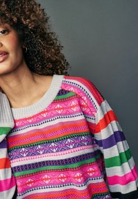 Pulover tricotat multicolor, cu modele roz, portocalii, violet și verzi, având un guler gri cu textură ribbed și un design lejer.