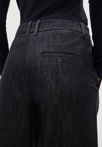 Tumši zili džinsa bikses ar fakturētu virsmu, ar diskrētu aizmugurējo kabatu un pogu detaļu. Piegrieztas, ar jostas cilpām.