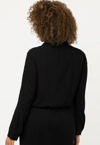 Sort langærmet top med krave, der har et cropped design og knapmanschetter. Glat stof med mat finish.