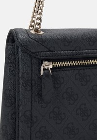 Sorte tekstureret håndtaske med subtil monogrammønster, guld lynlås og dragetab, samt guld kædistrap fastgjort til det øverste hjørne.