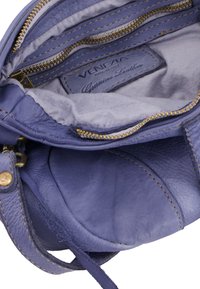Lila Lederhandtasche mit Innenraum, der mehrere mit Reißverschluss versehene Taschen aufweist, glatte Oberfläche und goldene Nähte. Das Etikett trägt die Aufschrift "Echtes Leder."