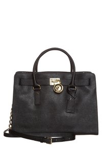 Sac à main synthétique noir avec quincaillerie dorée, design structuré, doubles anses et une bandoulière ajustable. Présente un charme logo et une finition texturée.