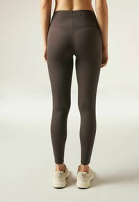 Leggings taille haute de couleur gris foncé, en tissu extensible ; design ajusté avec un logo discret à l'arrière, associés à des baskets claires.