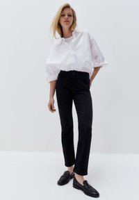 Pantaloni in denim nero con taglio dritto, abbinati a una camicia bianca over-size con bottoni. Texture morbide e design minimalista.