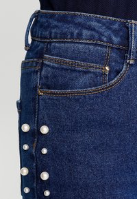 Jeanskjol med pärldetaljer längs sidan, i en mörkblå färg, texturerad tyg och orange sömmar i midjan och vid sömmarna.