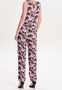 Jumpsuit floral con fondo negro, vibrantes flores rosas y verdes, diseño sin mangas y detalle de apertura en la espalda.