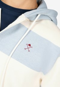 Katoenen hoodie met lichtblauwe en crèmekleurige horizontale strepen, met een rood geborduurd logo op de borst en een capuchon met trekkoord.
