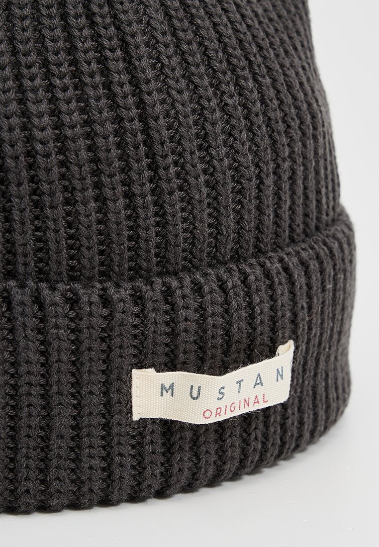 Ciemnoszara dziana czapka z prążkowanym wzorem, z kremową metką z napisem "MUSTAN ORIGINAL" w niebieskich i czerwonych literach.