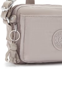Borsa a tracolla grigia in nylon con finitura testurizzata, dotata di una tasca frontale, di una toppa con logo rotondo e di un piccolo charm a forma di scimmia.