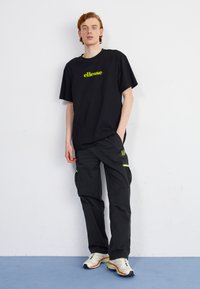 Čierne nadmerné tričko s neonovo zeleným logom "ellesse", skombinované s čiernymi cargo nohavicami s zelenými akcentmi a bočnými vreckami.