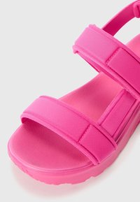 Różowe sandały z szerokimi paskami materiałowymi i grubą, wyściełaną podeszwą. Projekt charakteryzuje się gładką fakturą oraz profilowaną wkładką dla większego komfortu.