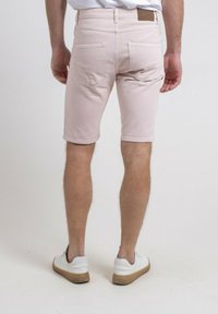 Shorts en denim rose clair avec une coupe slim, cinq poches et un ourlet court, associés à des baskets blanches avec des accents gris.