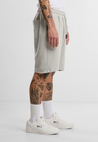 Lys grå bomullsshorts med snøring i livet, sidelommer og en lett slitt utseende. Brukt sammen med hvite sneakers og ankelsokker.
