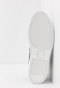 Baskets noires avec un dessus en tissu texturé et une semelle en caoutchouc blanc. Présente un branding subtil sur la semelle et une forme lisse et courbée.