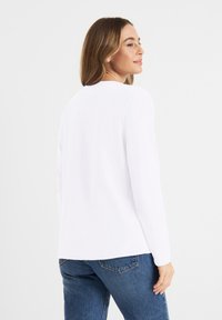 Witte lange mouwen shirt gemaakt van katoen, met een ronde halslijn en een eenvoudige ontwerp. Het shirt is gecombineerd met blauwe spijkerbroek.